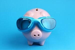 Piggy bank wearing blue swimming goggles against a bright blue background, symbolizing savings and cost-effectiveness in plumbing repairs to prevent increased water bills.