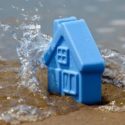 Blue toy house partially submerged in water with splashes, representing home and property care solutions.