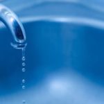 "Close-up view of a water faucet with droplets over a blue sink, highlighting plumbing maintenance".