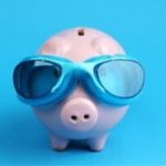 Light pink piggy bank with blue goggles against a bright blue background, representing playful savings for plumbing repairs.