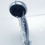 Sleek metallic showerhead with water flowing, highlighting plumbing maintenance for home cleanliness.