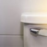 Classic toilet with rounded tank and chrome flush handle in a clean, light-colored bathroom by Bud's Plumbing.