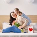 Woman and girl holding a bouquet and gift box in a cozy setting, symbolizing love and appreciation for plumbing services.