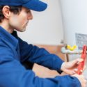 Technician in blue uniform repairing plumbing equipment and water heater for Bud's Plumbing in Evansville, IN.