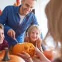Adult male and two children carving pumpkins indoors for Halloween, showcasing family creativity and festive decor.