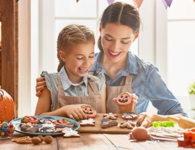 Mother and daughter decorating Halloween-themed cookies, showcasing festive treats and a cozy kitchen setting, emphasizing fall baking activities.