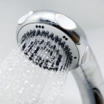 Showerhead with chrome finish and multiple spray settings, showcasing water droplets for modern bathroom plumbing solutions.