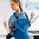 Woman in blue overalls with a plunger and blueprint in a modern kitchen for Bud's Plumbing & Repair Service.