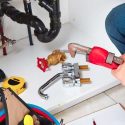 Hands using a pipe wrench in an organized plumbing workspace with tools for Bud's Plumbing & Repair Service.