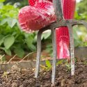 Red rubber boot beside garden fork in soil with green plants, representing gardening for homeowner plumbing services.