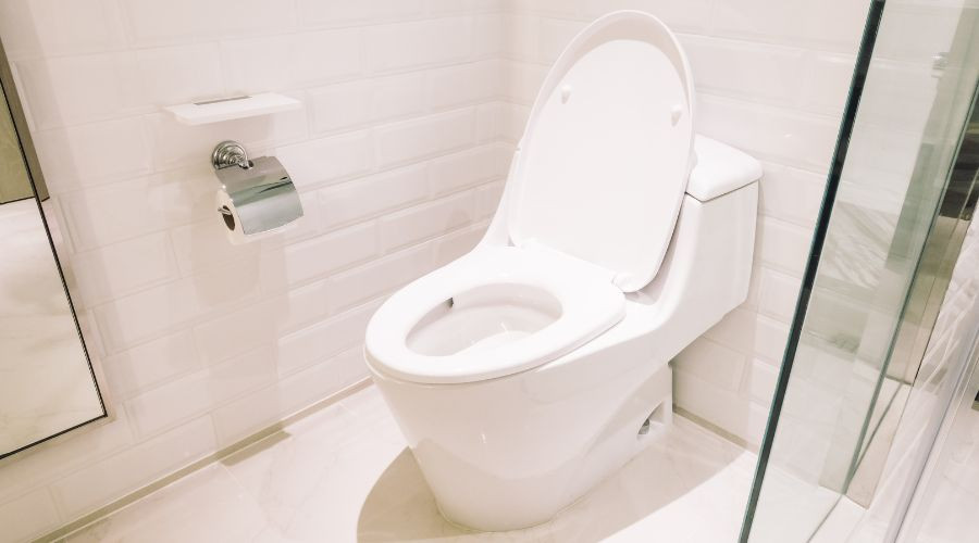 Modern toilet in a minimalist bathroom with wall-mounted toilet paper holder and glass shower enclosure by Bud's Plumbing.