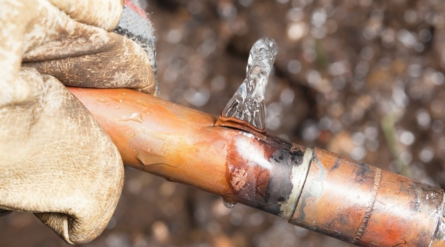 Copper pipe with a visible leak, showing water dripping, representing plumbing issues related to water leak detection and repair services.